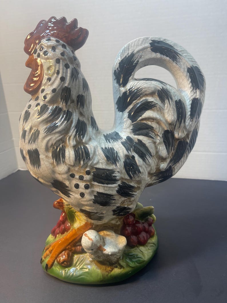 Pode incluir: Estatueta de galo de cer&acirc;mica com corpo salpicado branco, preto e cinza, crista e barbela vermelhas e cauda curva. A base apresenta uvas e um p&aacute;ssaro pequeno. O galo &eacute; um item decorativo.