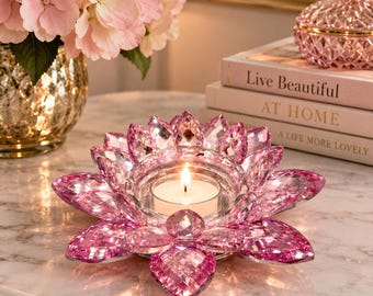 Pode incluir: Um suporte de vela em cristal rosa com formato de flor de lótus e design de pétalas facetadas. O centro contém uma pequena vela branca. O objeto é feito de vidro rosa transparente que reflete a luz, criando uma aparência cintilante.