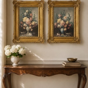 May include: Two rectangular oil paintings in ornate gold frames featuring floral arrangements in vases. The artwork depicts colourful bouquets of flowers against a dark background, displayed side by side on a wall above a wooden console table.