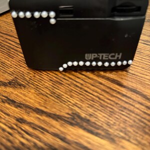 May include: A black and white camera with a white lens and a silver trim. The camera has a silver button on the top and a silver button on the side. The camera has a silver inscription that reads "UP-TECH". The camera is decorated with white rhinestones.