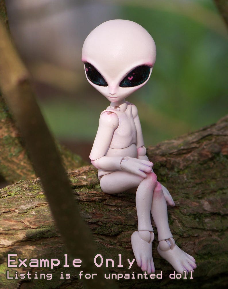 May include: A pale pink alien doll with large black eyes and pink accents, sitting on a tree branch. The doll has articulated joints and is unpainted. The text "Example Only" and "Listing is for unpainted doll" is visible.
