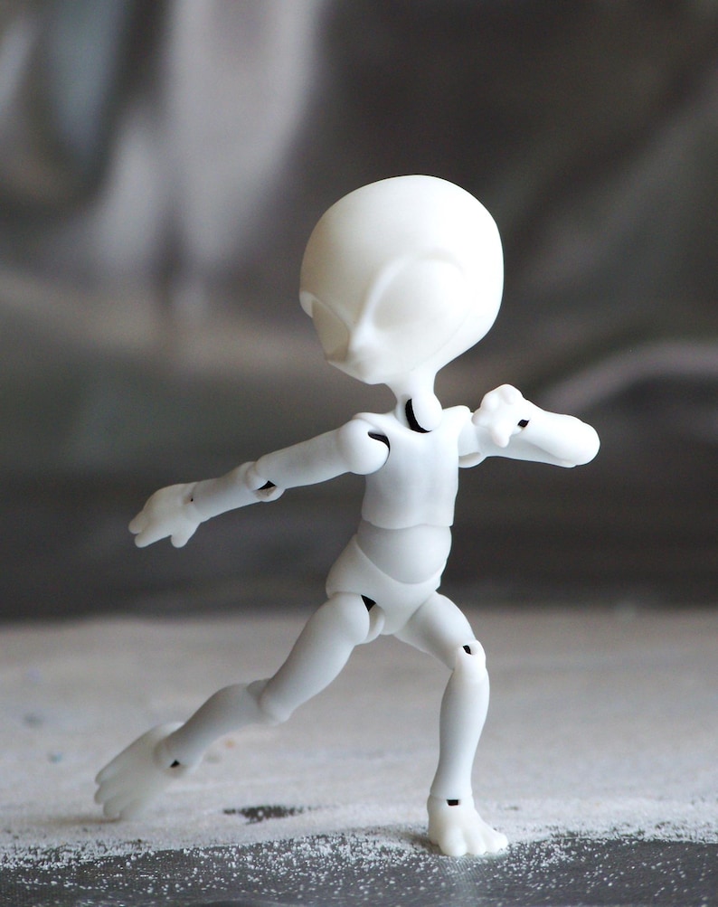 May include: A white articulated doll in a running pose. The doll has a smooth, rounded head and a slender body with visible joints at the elbows, knees, and ankles. The doll's arms are outstretched, and its legs are bent in a running motion.