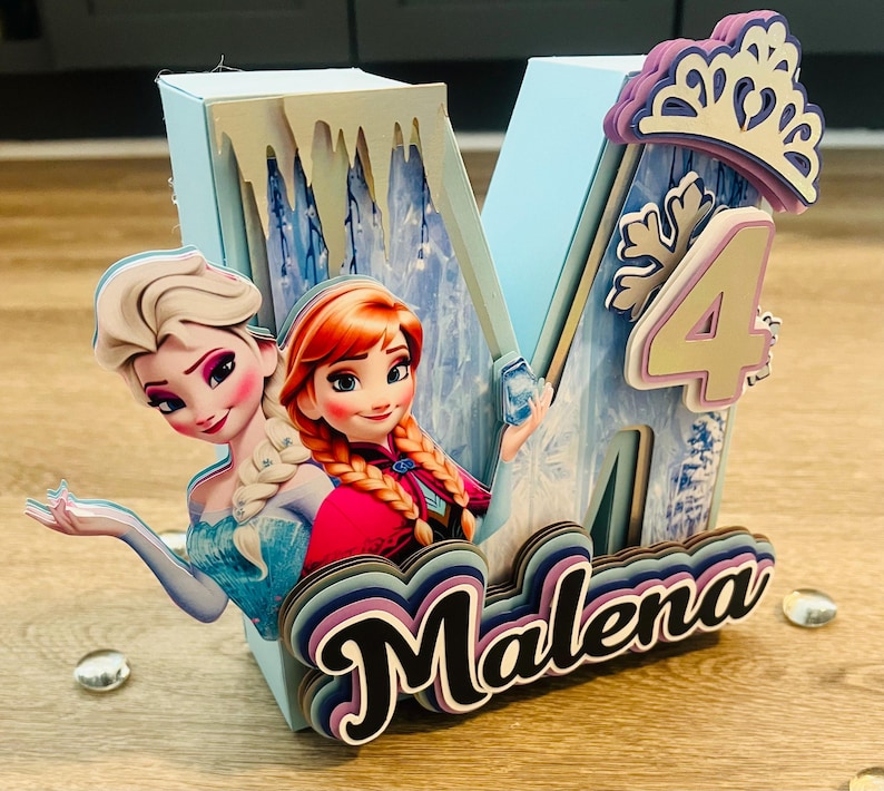 May include: A light blue, layered letter "M" with the name "Malena" in a cursive font. The letter features images of Elsa and Anna from Frozen, a number "4", and a crown. The design is for a birthday.