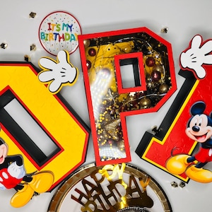 Könnte beinhalten: Bunte Geburtstagsdekoration mit den Buchstaben "OP" in Gelb und Rot, im Mickey Mouse-Design. Enthält Mickey Mouse-Figuren, weiße Handschuhe und ein "Happy Birthday"-Schild. Das "P" ist mit Lichtern gefüllt.