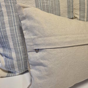 May include: Two throw pillows, one with a white and blue striped pattern and the other a solid white. The white pillow has a zipper closure on the back.