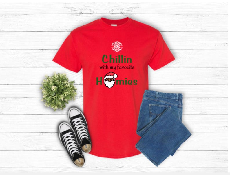K&ouml;nnte beinhalten: Ein rotes T-Shirt mit dem Text "Chillin with my favorite Homies" und einer Weihnachtsmann-Grafik. Das Shirt wird mit einer blauen Jeans und schwarz-wei&szlig;en Turnschuhen kombiniert. Eine kleine gr&uuml;ne Pflanze ist ebenfalls im Bild.