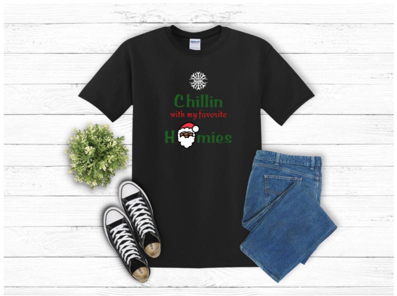 K&ouml;nnte beinhalten: Schwarzes T-Shirt mit dem Text "Chillin with my favorite Homies" in Gr&uuml;n und Rot. Das T-Shirt zeigt eine Weihnachtsmann-Grafik. Das Bild enth&auml;lt auch blaue Jeans und schwarz-wei&szlig;e Turnschuhe.