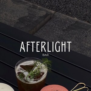 May include: A black table with the text "AFTERLIGHT BAR" in white lettering. A glass of iced tea with a sprig of dill is on the table.