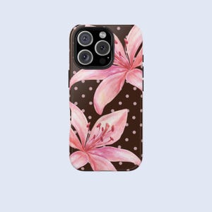 May include: A phone case featuring a watercolor design of pink lily flowers on a dark brown background with white polka dots. The case has a black camera module.