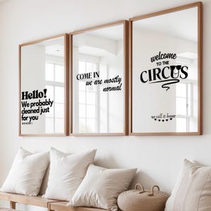 Può includere: Tre specchi rettangolari con cornici in legno sono montati su una parete bianca. Ogni specchio ha un testo nero. Il testo sugli specchi recita: "Hello! We probably cleaned just for you", "Come in we are mostly normal", e "Welcome to the Circus, we call it home."