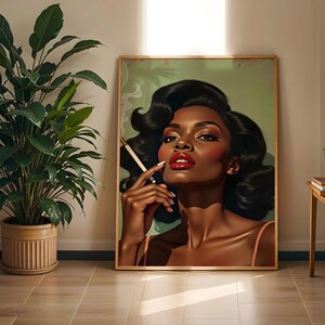 May include: A framed art print depicting a woman with dark skin, red lipstick, and black hair holding a cigarette. The artwork has a vintage aesthetic, with a soft green background and a wooden frame. The woman is wearing a light pink top.
