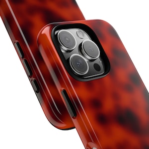 May include: A red and brown tortoiseshell phone case with a black camera bump and three lenses.
