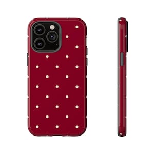May include: A red phone case featuring a white polka dot design. The image shows the case from the front and side, detailing the pattern and camera aperture. The case is designed to protect the phone.