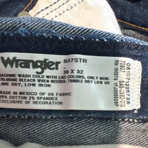 May include: Close-up of a Wrangler jeans label. The label is white with black text, indicating the brand, style, and size (30 x 32). It also includes washing instructions and fabric details: 98% cotton, 2% spandex.