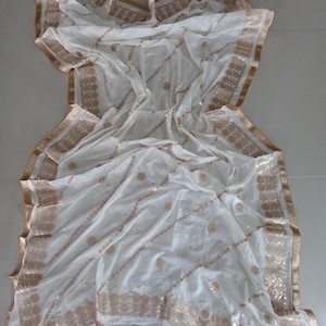 May include: A cream and ivory sheer scarf with gold embroidery and sequins. The scarf has a fringed edge and a tassel.