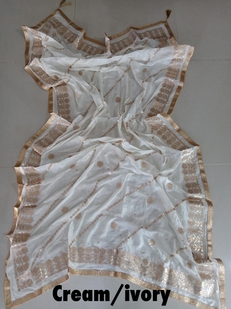 May include: A cream and ivory sheer scarf with gold embroidery and sequins. The scarf has a fringed edge and a tassel.