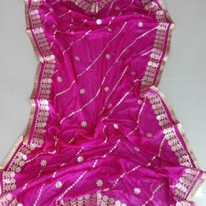 May include: A magenta silk dupatta with gold embroidery and a gold border. The dupatta has a floral design and is perfect for a special occasion.