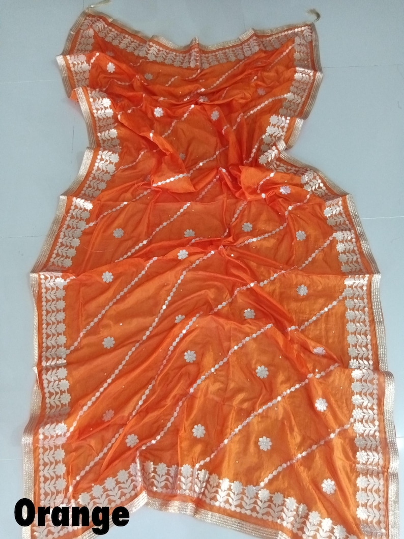 May include: Orange sheer fabric saree with silver and white embroidery. The saree has a floral design and a border with a paisley pattern.