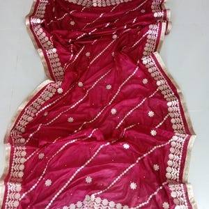 May include: A maroon or burgundy sheer dupatta with gold embroidery and a gold border. The dupatta has a floral design and is perfect for a special occasion.