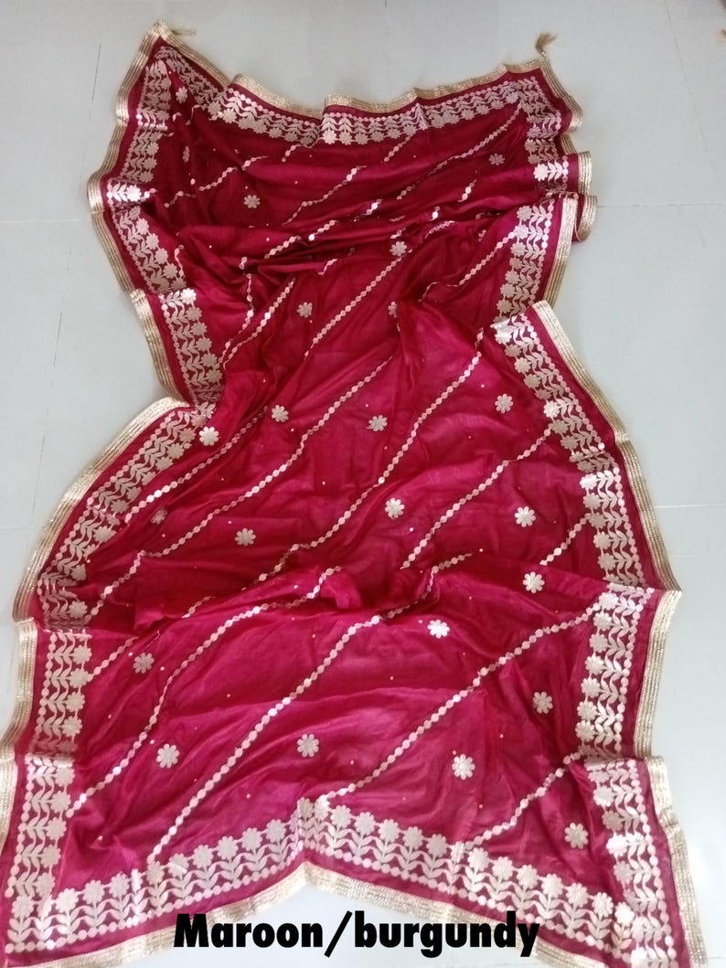May include: A maroon or burgundy sheer dupatta with gold embroidery and a gold border. The dupatta has a floral design and is perfect for a special occasion.
