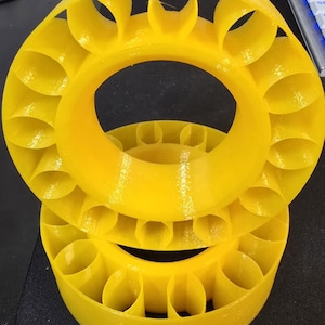 May include: Two bright yellow 3D printed rings with a series of evenly spaced holes around the outer edge. The rings are stacked on top of each other.