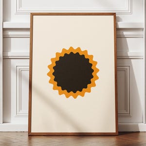Op de afbeelding: Een ingelijste kunstdruk met een minimalistisch ontwerp. Het kunstwerk toont een zwarte cirkel met een geschulpte oranje rand op een crèmekleurige achtergrond. De houten lijst wordt gepresenteerd op een houten vloer. De print is een decoratief stuk.