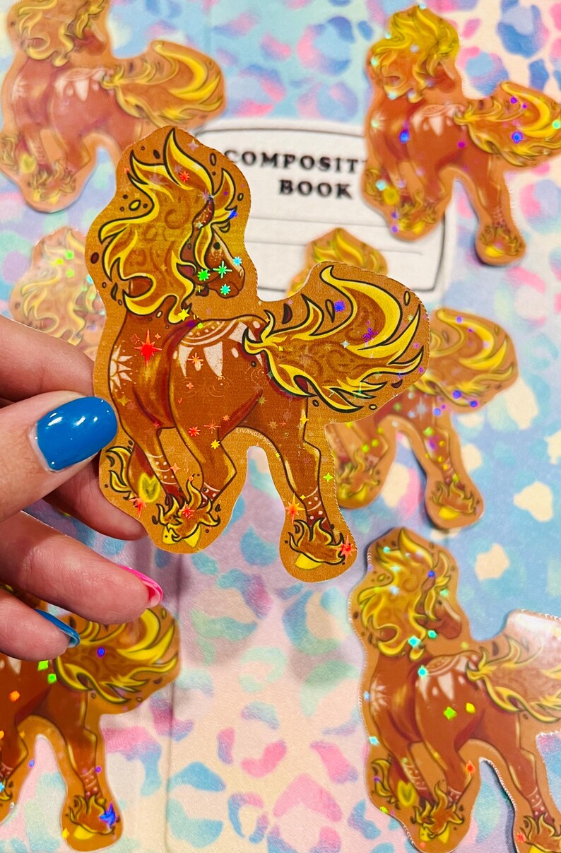 May include: Holographic stickers featuring a stylized horse with a flowing mane and tail. The stickers are primarily brown and gold with iridescent accents. The text "COMPOSIT BOOK" is visible in the background. These stickers are ideal for scrapbooking and crafts.