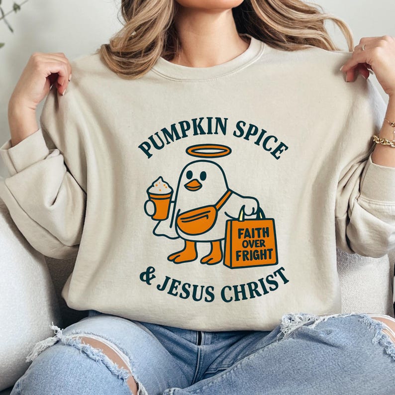 May include: Beige sweatshirt with a graphic of a cartoon bird wearing a fanny pack and holding a coffee cup and shopping bag. Text reads "Pumpkin Spice & Jesus Christ" in green.