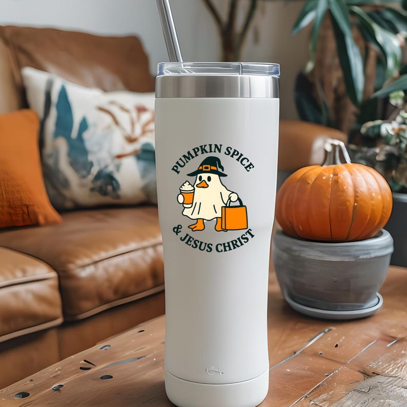 May include: A white insulated tumbler with a silver lid and straw. The tumbler features a graphic of a ghost wearing a hat and holding a coffee cup and a shopping bag. The text on the tumbler reads "PUMPKIN SPICE & JESUS CHRIST."