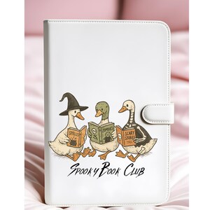 May include: White tablet case with a cartoon illustration of three ducks reading books. The books are titled "Spells", "Zombies", and "Scary Stories". The ducks are in Halloween costumes. The text "Spooky Book Club" is below the illustration.