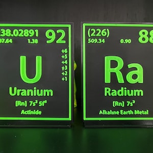 Può includere: Due blocchi di elementi della tavola periodica neri e verdi. Il primo blocco mostra l'uranio (U) con il numero atomico 92 e il peso atomico 238,02891. Il secondo blocco mostra il radio (Ra) con il numero atomico 88 e il peso atomico (226).