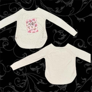 Könnte beinhalten: Zwei cremeweiße Langarmpullover mit strukturiertem Rosenmuster. Der obere Pullover hat einen rechteckigen Aufnäher auf der Brust, der zwei illustrierte Teddybären umgeben von rosa Blumenakzenten und einer Herzform zeigt.