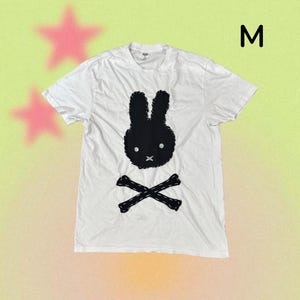 Puede incluir: Camiseta blanca con un diseño de cara de conejo negro y huesos cruzados. La camiseta tiene cuello redondo y mangas cortas. La letra "M" es visible en la esquina superior derecha.