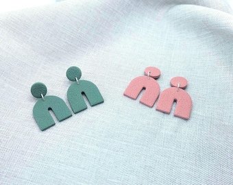 May include: Two pairs of polymer clay earrings. One pair is teal green and the other pair is dusty rose. Both pairs are shaped like arches.