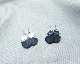 May include: A pair of black and white statement earrings with a geometric design. The earrings are made of polymer clay and have a matte finish.