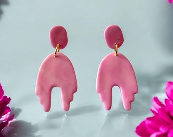 May include: A pair of pink polymer clay earrings with a dripping, abstract design. The earrings are a light pink color with a subtle marbled effect.