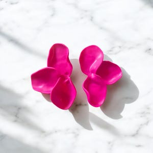 Może przedstawiać: Para różowych kolczyków w kształcie kwiatów. Każdy kolczyk składa się z trzech nakładających się płatków.