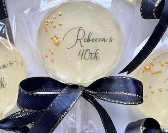 May include: Clear, round lollipops with gold-colored sprinkles are packaged in clear plastic. Each lollipop is decorated with the text "Rebecca's 40th". The lollipops are tied with navy blue ribbon with gold trim.