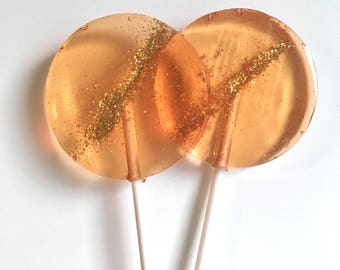 May include: Two round lollipops with gold glitter embedded in the orange candy. The lollipops are on white sticks.