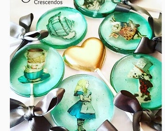 May include: Assortment of round and heart-shaped lollipops with various Alice in Wonderland themed images, including the Mad Hatter, the Cheshire Cat, and Alice herself. The lollipops are decorated with silver ribbons and are on a white surface.