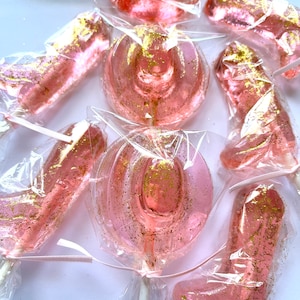 May include: Pink and gold glitter lollipops shaped like cowboy hats and boots. The lollipops are individually wrapped in clear plastic.