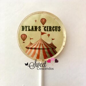 Może przedstawiać: Okrągły lizak z białym tłem i kolorowym wzorem namiotu cyrkowego. Tekst "Dylan's Circus" jest nadrukowany czarnymi literami na lizaku.