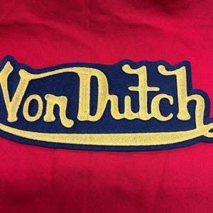 May include: A navy blue embroidered patch with the text "Von Dutch" in gold thread.