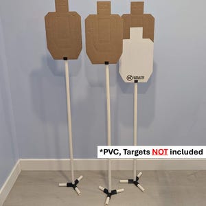 Könnte beinhalten: Drei Zielscheibenständer mit weißen Stangen und schwarzen Basen. Die Zielscheiben sind nicht enthalten. Zwei Zielscheiben sind braun, eine ist weiß mit dem Text "KRATE". Der Text "*PVC, Targets NOT included" ist sichtbar.
