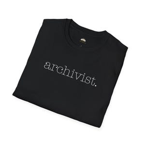 May include: Black t-shirt with the word "archivist" printed in white. The shirt is folded, showing the front, and appears to be made of a soft material. The neckline has a small tag.