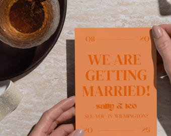 Puede incluir: Una tarjeta de invitación de boda naranja sostenida por manos. La tarjeta dice "WE ARE GETTING MARRIED!" con los nombres "sally & leo" y la fecha "08-20-20" y "20-25". Una bebida y elementos decorativos están en el fondo.