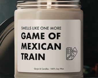 May include: A beige candle with a black label that reads "Smells like one more Game of Mexican Train". The label also features a black and white illustration of a domino. The candle is in a clear glass jar with a black lid.