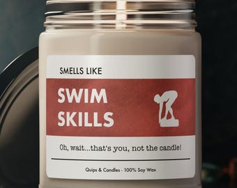 May include: A brown glass candle jar with a white label that reads "Smells Like Swim Skills" and a red silhouette of a swimmer. The text on the label also reads "Oh, wait...that's you, not the candle!" and "Quips & Candles - 100% Soy Wax".