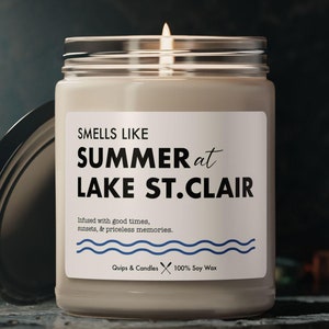 May include: A beige candle with a white label that reads "SMELLS LIKE SUMMER at LAKE ST.CLAIR" and "Infused with good times, sunsets, & priceless memories." The label also includes the text "Quips & Candles X 100% Soy Wax".