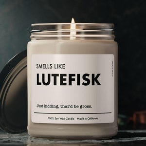 May include: A white soy wax candle in a glass jar with a black label that reads "SMELLS LIKE LUTEFISK Just kidding, that'd be gross. 100% Soy Wax Candle Made in California".
